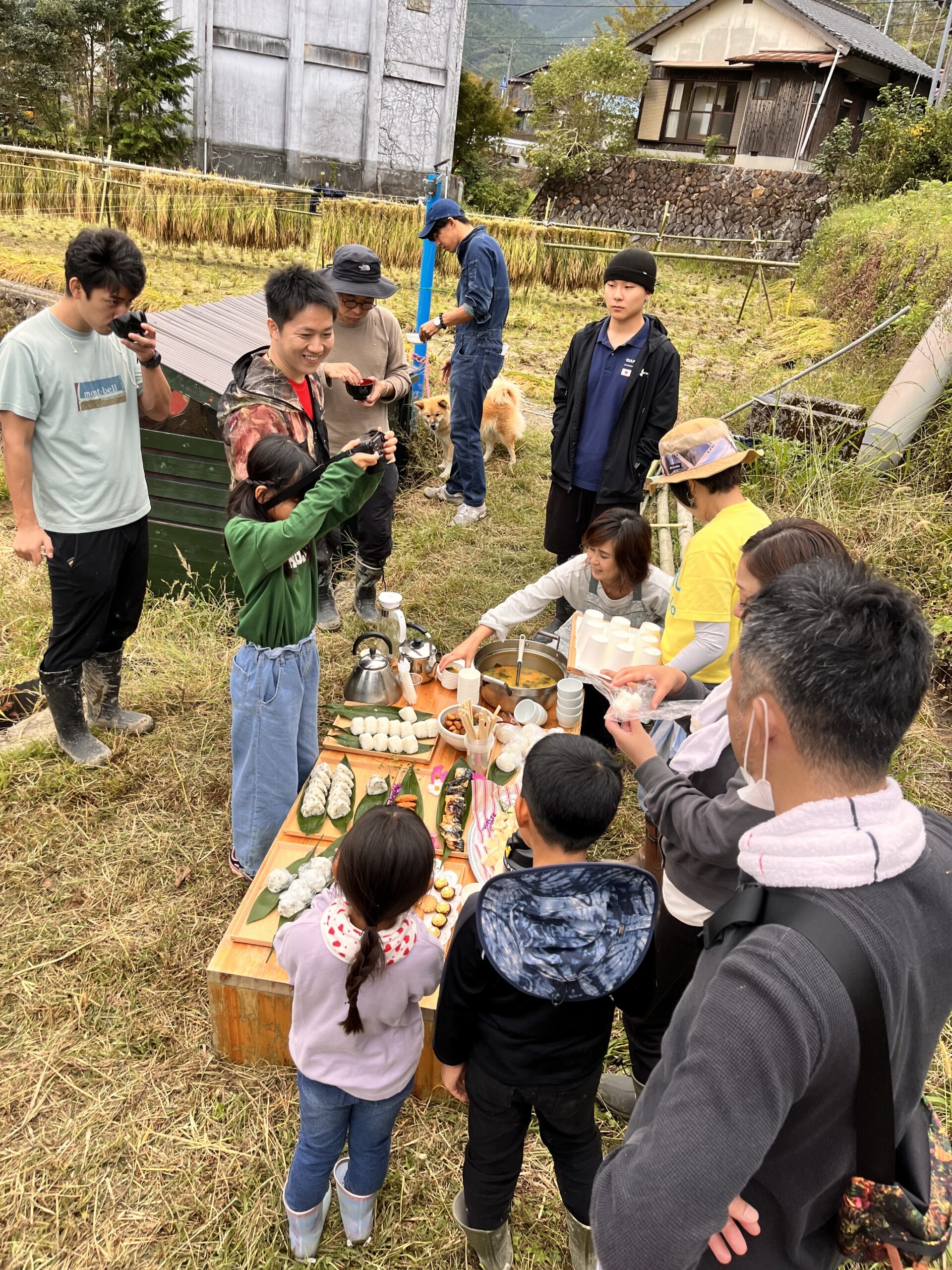 稲を干した田んぼのそばで、食卓を囲む参加者たち